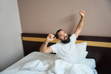 Neşeli adam aydınlık bir otel odasında uyanır, oda temiz ve rahattır.