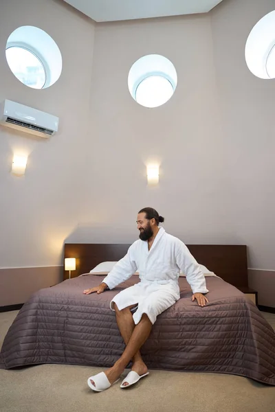Мужчина Халате Сидит Большой Кровати Гостиничном Номере Круглые Окна Помещении — стоковое фото