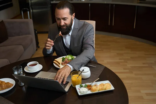 Bärtiger Mann Frühstückt Hotelzimmer Ein Funktionierender Laptop Liegt Auf Dem — Stockfoto