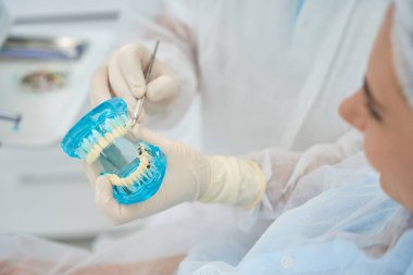 Doktor ortodontist, hastaya diş implantı ve kaplaması olan koruyucu eldivenli bir model gösteriyor.