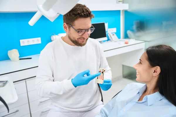 Усміхнений Стоматолог Уніформі Тримає Модель Зубів Пояснює Пацієнтці Він Буде — стокове фото