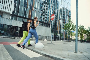 Genç bir çift, konuşuyor, yaya geçidi boyunca yürüyor, yol tabelasının yanında.