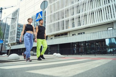 Genç bir çift, el ele tutuşmuş, yaya geçidi boyunca yürüyorlar, yol işaretinin yanında.