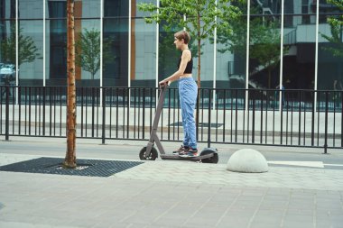 Genç gayri resmi kız kaldırımda scooter sürüyor, dişi ince ve kısa saçlı.