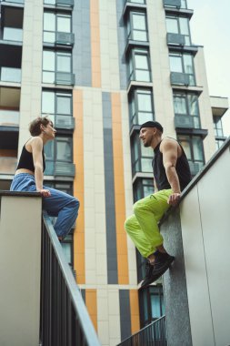 Genç erkek ve kız arkadaşı büyük modern binaların yanındaki yüksek kaldırımda dinleniyorlar.