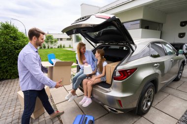 Çocuklu bir çift yeni ve modern bir eve taşınır. Erkek, içinde eşyalar olan bir kutu taşır.