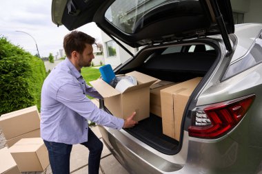 Arabadan yeni bir eve kutular taşıyan bir adam. Bahçede yeşil bir çimen.