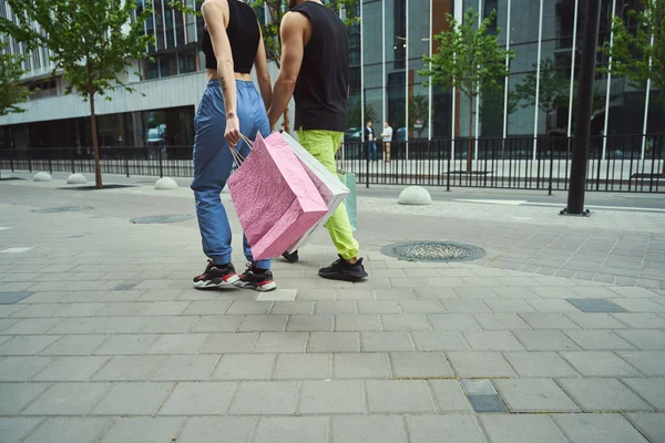 年轻夫妇手牵手走在人行道上 人们都有购物袋 — 图库照片