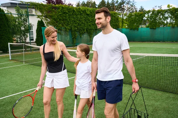 Happy family of three walks on the tennis court, they have tennis rackets in their hands