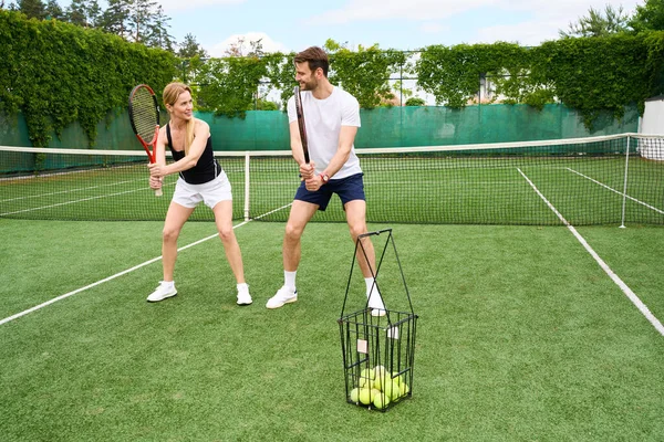 男と女がテニスラケットを手に持っている テニスボールのバスケットが近くに立っている — ストック写真