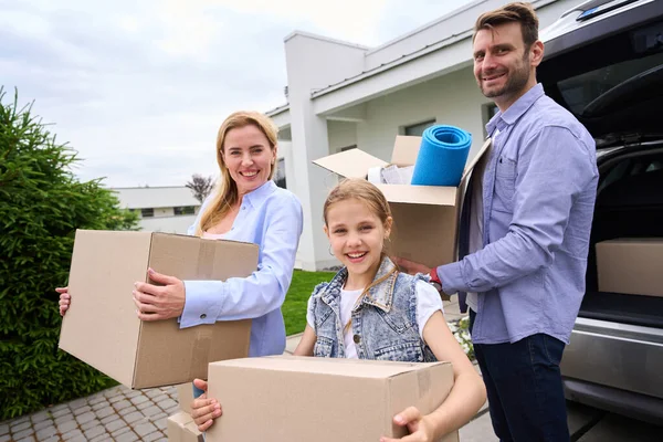 10代の娘と結婚したカップルは新しい現代的な家に移動し 人々は物を持って箱を運びます — ストック写真