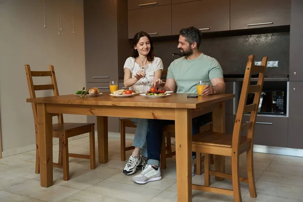 ハッピーな配偶者は木製のテーブルで居心地の良いキッチンで朝食を介して通信します — ストック写真