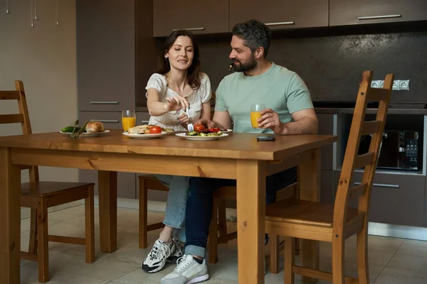 カップルは木製のテーブルで居心地の良いキッチンで朝食を持っています 人々は良い気分です — ストック写真