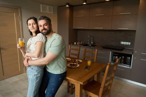 かわいい配偶者は立って お互いに抱き合って 台所の自宅で 朝食は木のテーブルで提供されます — ストック写真