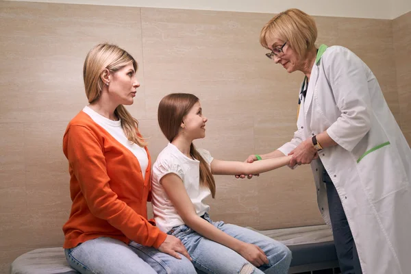 小児科オフィスの受付で医師がオレンジ色のセーターで小さな患者 少女の母親を診察する — ストック写真