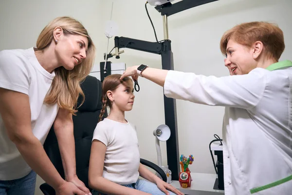 診療所の医師は 子供の母親の隣の若い患者の視力をチェックする — ストック写真