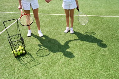 Genç bir kadın ve bir kız tenis kortunda, dişi çocuğun elini tutuyor.