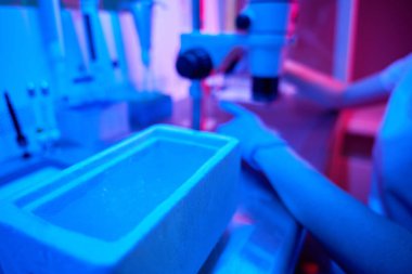 İş yerindeki kadın laboratuvar asistanı güçlü bir mikroskop ve sıvı nitrojen tankı kullanıyor.