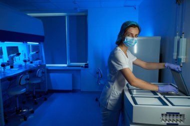 Tıbbi üniformalı bir kadın, biyolojik materyali olan bir konteynırı dondurucu odaya gönderir. Uygun koşullar sağlanır.