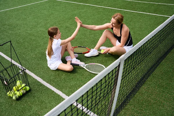 十代の少女と彼女の母親はテニスコートの芝生で通信し 彼らはボールのテニスラケットとバスケットを持っています — ストック写真