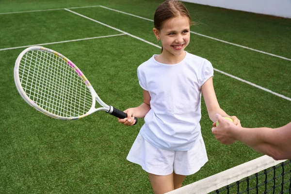 若いテニスプレーヤーは若い女性の手からボールを取ります 少女は彼女の手にテニスラケットを持っています — ストック写真