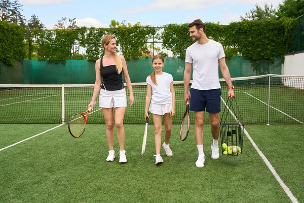 ティーンエイジャーの娘がテニスコートを歩いていて テニスラケットを手に持っている — ストック写真