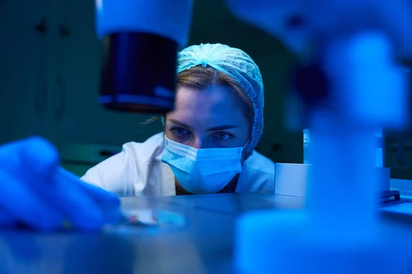 Laboratory assistant in a protective mask conducts an ICSI procedure, micromanipulator set is used in the work