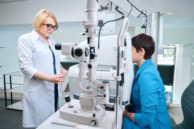 Gülümseyen optometrist, danışma sırasında yetişkin kadın müşteride otomatik nesnel kırılma gerçekleştiriyor