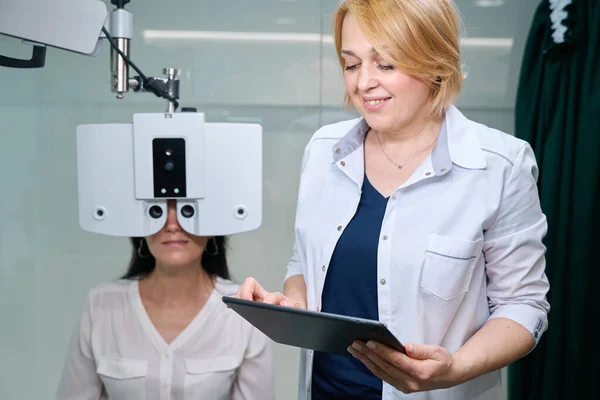 病人坐在检查椅上 通过平板电脑上眼科医生监测的数字视光镜进行检查 — 图库照片