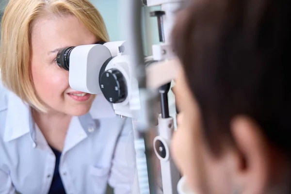 Doświadczona Biała Okulistka Patrząca Przez Mikroskop Lampy Szczelinowej Oczy Pacjenta — Zdjęcie stockowe