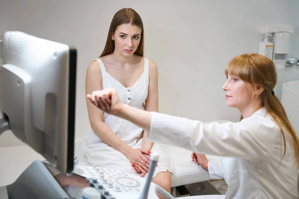 女性の医者は超音波部屋の若い女性に相談します 超音波の医者は超音波機械のモニターを指します — ストック写真
