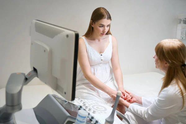 女性の医学は超音波部屋の若い女性と暖かく伝達し 医者は患者の手を握ります — ストック写真