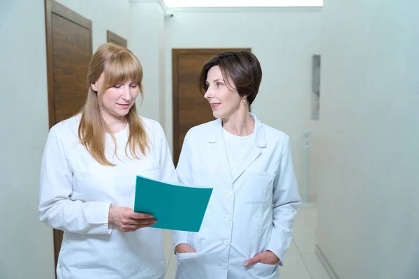 Female doctors walk along the hospital corridor, they have a blue folder with documents