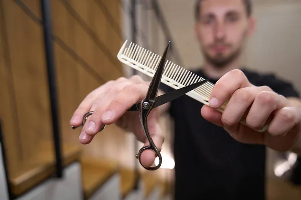 Barber man holding scissors and comb in hands, barbershop minimalist interior
