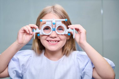 Portrait of cheerful little girl with ophthalmic trial frame on face looking in front of her clipart