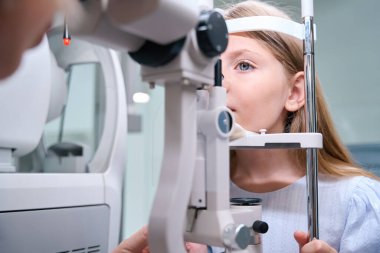 Çocuk, başını çene ve alın desteğine yaslarken lamba demetine bakıyor.