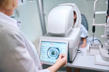 Otomatik fraktör dokunmatik ekranda pediatrik hasta göz görüntüsüne bakan kadın optometrist