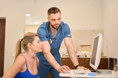 Sandalyeye oturmuş bilgisayar ekranına bakan kadın, özel testler yapan erkek doktor algılarını ve anlayışını kontrol eden, rutin atletlerin akıl sağlığı kontrolleri