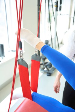 Modern odada kırmızı kablo kullanarak antrenörle askıya alma terapisi yapan beyaz bir kadın.