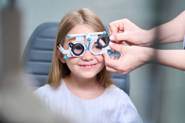 Optometrist hands inserting spherical lenses into ophthalmic trial frame cells on little girl face