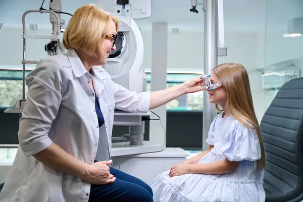 女性眼科医 クロスシリンダーを微笑む少女の顔に光学試験フレームに取り付ける — ストック写真