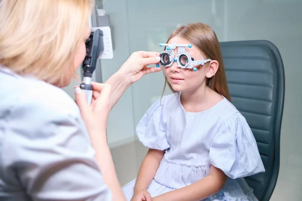 小さな女の子の顔にレンズを球状の試験フレームセルに挿入しながら 網膜鏡を通して見るオルタノプティスト — ストック写真