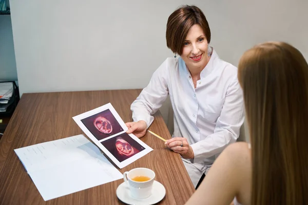 2人の女性が一緒に胎児の超音波画像を見て 女性はお茶の上に暖かくコミュニケーションします — ストック写真