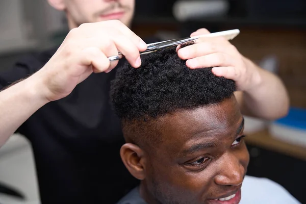 Hairdresser uses scissors and a comb in his work, his client has curly hair