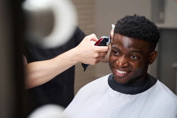 Lächelnder Afroamerikaner Sitzt Einem Friseurstuhl Der Meister Macht Ihn Mit — Stockfoto