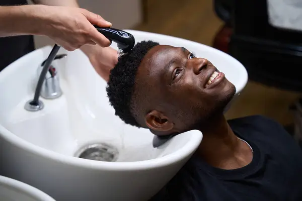 Hairdresser washes the guys hair in a special sink, and his African American client curly hair