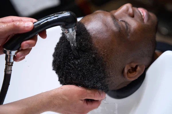 Barber washes the clients hair in a special sink, the African American male has curly hair