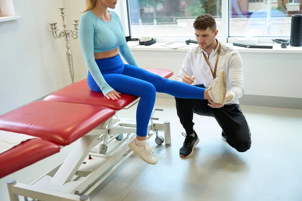 现代房间内女病人的集中健身教练检查腿 — 图库照片