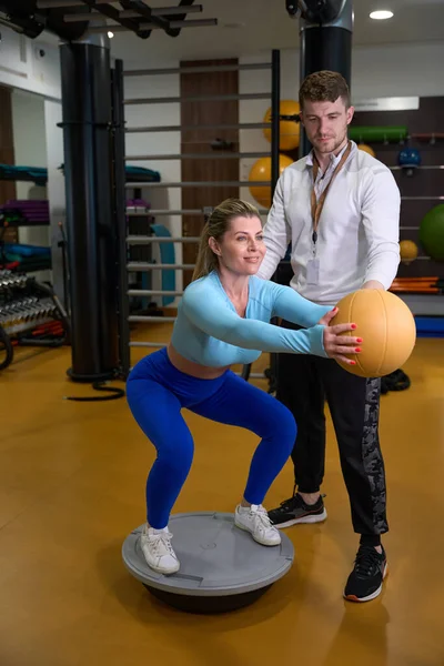 做仰卧起坐的女运动员 手拉着球 抽动腿和臀部肌肉 教练支持体操病人 — 图库照片