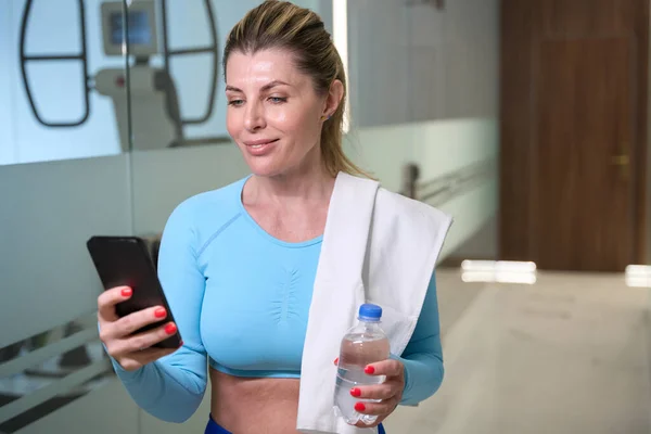 Sports woman checking her pulse and blood pressure on smartphone application, entering work-out data for watching out progress, gym workout